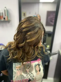 Warm brunette hair with golden caramel highlights and bouncy curls, styled by the Bognor Regis colour experts.