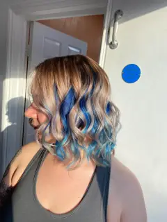 Blonde curls with bold royal blue peek-a-boo highlights, a creative look from our Bognor Regis hair specialists.